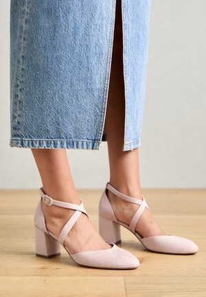 Lyserøde lukkede hæle med blokhæl og korsremdesign. Fremstillet af materiale med ruskindslignende overflade, der har en glat tekstur og minimal detaljering.