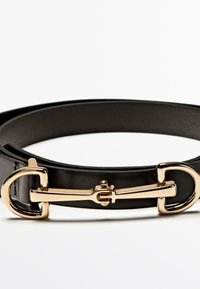Ceinture en cuir noir avec une boucle en métal doré. La boucle présente un design équestre distinctif et une finition lisse.