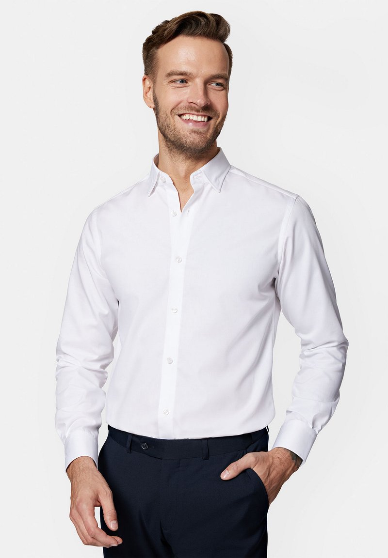 Biała koszula z długim rękawem i kołnierzykiem zapinanym na guziki, o gładkiej fakturze i ukrytym zapięciu, w zestawie z ciemnymi spodniami garniturowymi.