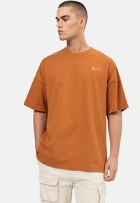 Krátky rukáv oranžové tričko vyrobené z bavlny, s okrúhlym výstrihom a malým bielym logom na ľavom hrudníku. Voľný strih.