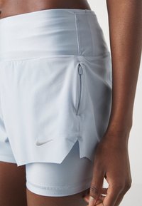 Helle blaue Sportshorts mit glatter Textur, seitlicher Reißverschlusstasche und einem silbernen Nike-Logo auf der unteren linken Seite.