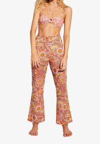 Ensemble deux pièces à motif floral comprenant un crop top noué et un pantalon évasé dans des teintes vives de rose, orange et jaune. Matière en coton.