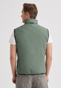 Green sleeveless vest with a high collar, made from lightweight material; features a smooth texture and black side panels.