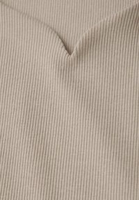 Beige tyg med en ribbad textur, som har en subtil V-formad veck. Mönstret består av jämnt fördelade vertikala linjer.