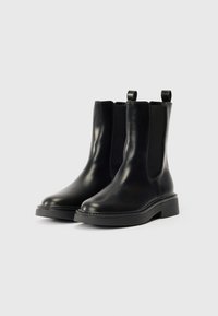 Crne kožne gležnjače s elastičnim bočnim panelima, zaobljenim prstima i ručkama za oblačenje. Debeli, strukturalni gumenjak pruža dodatno prianjanje i stabilnost.