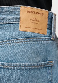 Κοντινή λήψη τσέπης ανοιχτού μπλε τζιν με καφέ δερμάτινη ετικέτα με την επιγραφή «JACK & JONES, Jeans Intelligence, Since 1990, Craftsmanship and Dedication.»