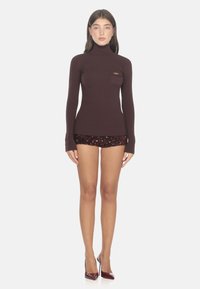 Bordeauxfarbener gerippter Rollkragenpullover mit langen Ärmeln und einer Brusttasche, kombiniert mit Pailletten-Shorts und glänzenden roten High Heels.