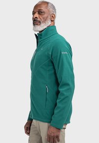 Türkiser Fleece-Jacke mit hohem Kragen, zwei seitlichen Reißverschlusstaschen und dezenten Nähten. Das Material wirkt weich mit einer strukturierten Oberfläche.