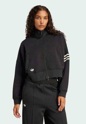 Svart kort zip-up sweatshirt med hög krage, framfickor och tre vita ränder på ärmarna. Har en liten logotyp på bröstet.