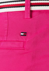 Pantaloni corti fucsia con un piccolo logo rettangolare sopra la tasca posteriore e una cintura a strisce rossa, bianca e nera.