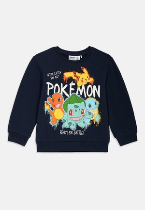 Tengerészkék pulóver színes Pokémon grafikával, amelyen Pikachu, Charmander, Bulbasaur és Squirtle látható, valamint a "KÉSZ A HARCRA!" felirattal.