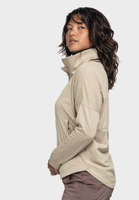 Beige Zip-up-Fleecejacke mit hohem Kragen, Seitentaschen und tailliertem Schnitt. Weiche Textur mit dezenten Steppnähten.