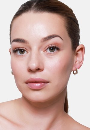 Orecchini a cerchio d'oro con piccoli cristalli trasparenti, indossati da una modella con pelle liscia, trucco leggero e capelli lisci su uno sfondo semplice.