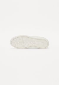 Suela de zapatilla blanca con una superficie de goma texturizada, detalles de patrón, un emblema circular y una banda de rodadura pronunciada para mayor agarre.