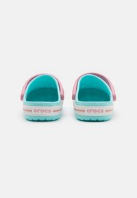 Two pairs of Crocs, featuring a pink heel strap and turquoise inner lining, with white and light blue outer soles and striped accents.