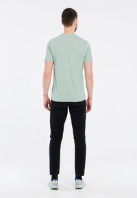 Jasnozielona koszulka krótki rękaw, dekolt okrągły, w połączeniu z czarnymi, dopasowanymi dżinsami i wielokolorowymi butami sportowymi. Prosta, gładka faktura.