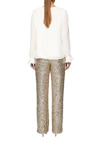Weißes Bluse mit gefalteten langen Ärmeln und Rüschenbündchen, kombiniert mit goldenen Pailletten-Hosen mit weitem Bein, die eine glatte Textur und einen glänzenden Finish haben.