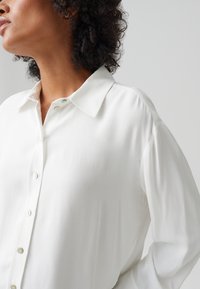 Weißes Hemd mit Kragen, aus weichem Stoff, mit Frontknöpfen und lässiger Passform, das die glatte Textur und das minimale Design betont.