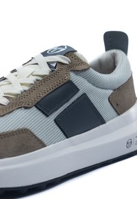 Sneaker med överdel i grått nätmaterial, bruna mockadetaljer, mörkblå läderlappar, vita snörningar och en vit sula med strukturerat svart mönster.