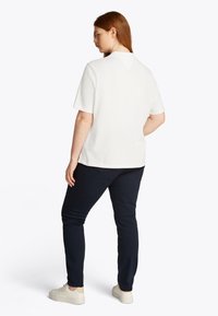 White short-sleeve shirt with a solid texture and back v-neck detail, paired with dark navy pants and white sneakers.