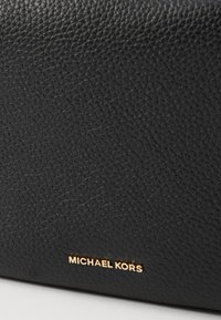 Black textured leather bag featuring a gold logo detailing. The surface has a pebbled pattern for added depth and interest.