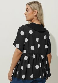 Blusa nera con pois bianchi, maniche corte, dettaglio del colletto sul retro, vita arricciata per una vestibilità rilassata, texture morbida.