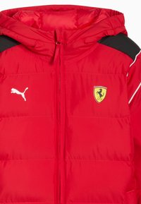 Czerwona kurtka puchowa z kapturem, czarne akcenty na ramionach, białe detale, logo Puma i żółty emblemat Ferrari. Teksturowana powierzchnia z pikowanym wzorem.