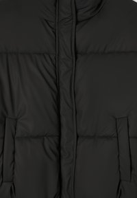 Czarna pikowana kurtka z obszyciem, z szerokimi pikowanymi sekcjami i pionowym szwem. Zawiera dwie boczne kieszenie.