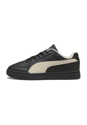 Baskets basses Puma noires et beiges avec lacets, bout perforé et marquage Porsche sur le côté et la semelle.