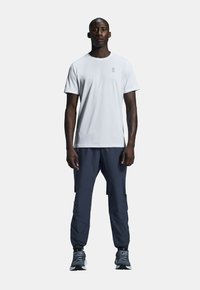 White short-sleeve athletic shirt with subtle logo, paired with navy cargo pants and grey running shoes. Smooth fabric and relaxed fit.