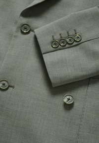 Világosszürke blazer, texturált anyagból. Kerek zöldes gombok díszítik az elejét és az ujja végét, kiemelve a szabott, struktúrált dizájnt.