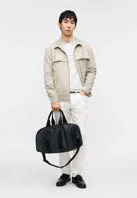 Μαύρη σακίδιος με σχέδια, διπλές λαβές και ρυθμιζόμενο ιμάντα ώμου, με φερμουάρ κλεισίματος και υφασμάτινες λεπτομέρειες.