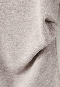 Détail d'un pull en tricot gris montrant une texture lisse, des fibres douces et des drapés délicats avec des variations subtiles de couleur sur le tissu.