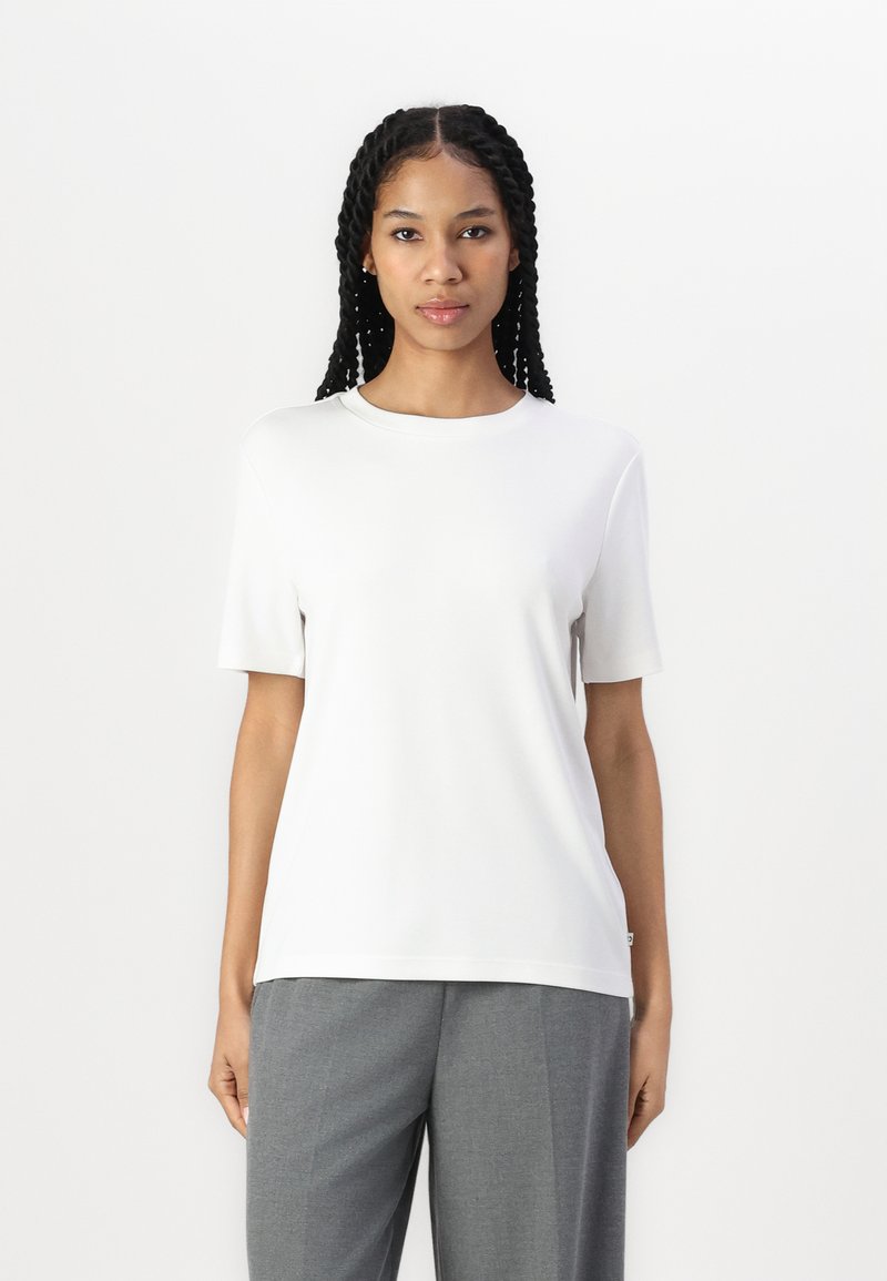 Vit kortärmad t-shirt i mjukt, lätt tyg med rund halsringning. Matcher grå högmidjade byxor.
