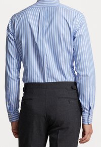 Camisa a rayas azul claro con líneas blancas, de mangas largas y puños con botones. Combinada con pantalones oscuros grises que tienen un bolsillo trasero.