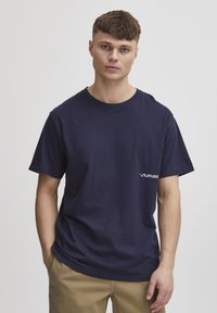 Marineblå bomulds T-shirt med korte ærmer, rund hals og lille hvidt logo tekst på venstre bryst. Casual pasform med en glat overflade.