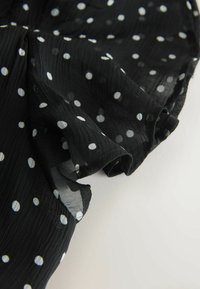 Črna prosojna tkanina z belimi pikami, ki ima na svetli podlagi nežne, rahlo nabrane robove.