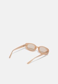 Ochelari de soare din plastic de culoare piersică deschisă, cu lentile ovale, brațe elegante și accente din metal argintiu. Lentilele sunt ușor nuanțate.