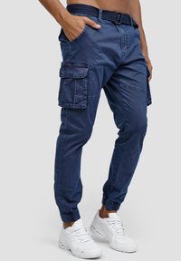 Pantalones cargo de la marina con puños elásticos, que cuentan con múltiples bolsillos, un cinturón y un ajuste relajado. La tela parece suave con una textura duradera.