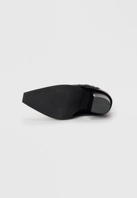 Black heeled shoe with a pointed toe, smooth leather upper, textured sole, and decorative accent near the ankle.