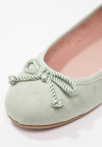 Ballerine en daim vert clair avec détail de nœud en corde torsadée et doublure intérieure rose, vue en gros plan de face.