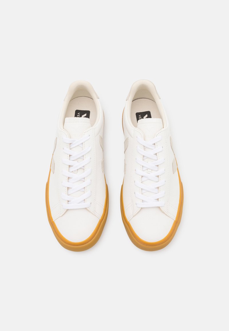 Baskets blanches en cuir avec semelle en caoutchouc orange. Présentent un design classique à lacets et des accents latéraux subtils. Texture lisse, style minimaliste.