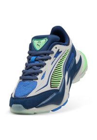 Sneaker Puma RS blu e bianche con lacci blu navy, dettagli verdi, inserti in rete e suola spessa, angolata per mostrare il lato anteriore e laterale.