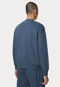 Felpa di cotone blu con scollatura a girocollo e polsini a coste, caratterizzata da una vestibilità rilassata e dettagli di cucitura discreti sulla schiena.