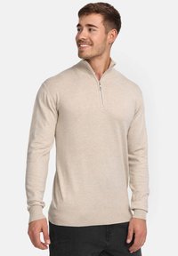 Maglione beige lavorato a maglia con mezza cerniera, maniche lunghe, polsini e orlo a costine, texture morbida e design aderente.