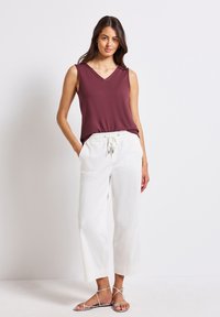 Burgundy ärmlös topp med V-ringning, parat med vita, lätta byxor med dragsko och platta sandaler med remmar.