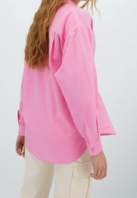 Getailleerde lichtroze blouse met lange mouwen, manchetknopen en een gebogen zoom. Gemaakt van een zachte, gestructureerde stof met lichte melering.