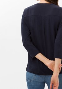 T-shirt à manches longues bleu marine avec un col rond, dotée d'une couture yoke à l'arrière et d'un tissu doux et lisse. Associée à un jean bleu.