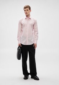 Ροζ πουκάμισο με μακριά μανίκια και κούμπωμα με κουμπιά, σετ με μαύρο παντελόνι και μαύρη τσάντα. Λείο ύφασμα, εφαρμοστή γραμμή και casual επίσημη εμφάνιση.