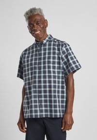 Kurzarm-Hemd aus Karo mit marineblauem und hellblauem Karomuster, Button-Down-Kragen, Brusttasche und einer entspannten Passform. Material aus Baumwollmischung.